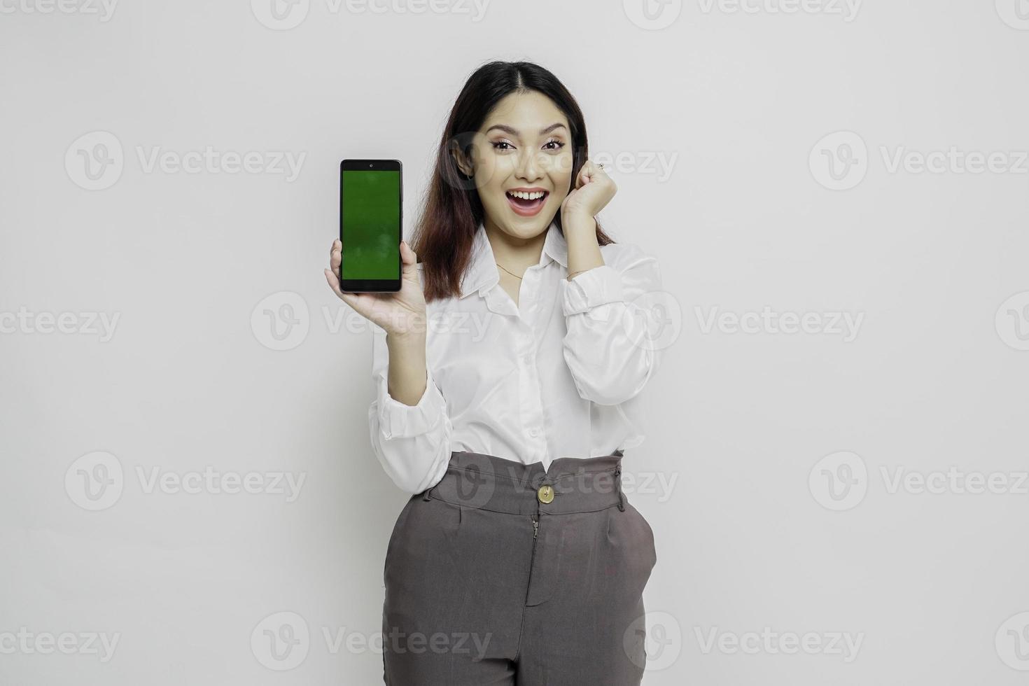 opgewonden Aziatisch vrouw vervelend wit overhemd richten Bij de kopiëren ruimte naast haar terwijl Holding haar telefoon, geïsoleerd door wit achtergrond foto