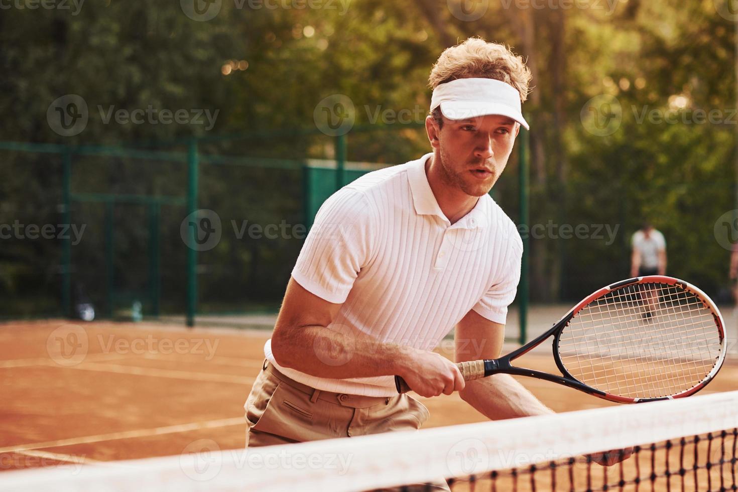 houdt racket in handen. jong tennis speler in sportief kleren is Aan de rechtbank buitenshuis foto