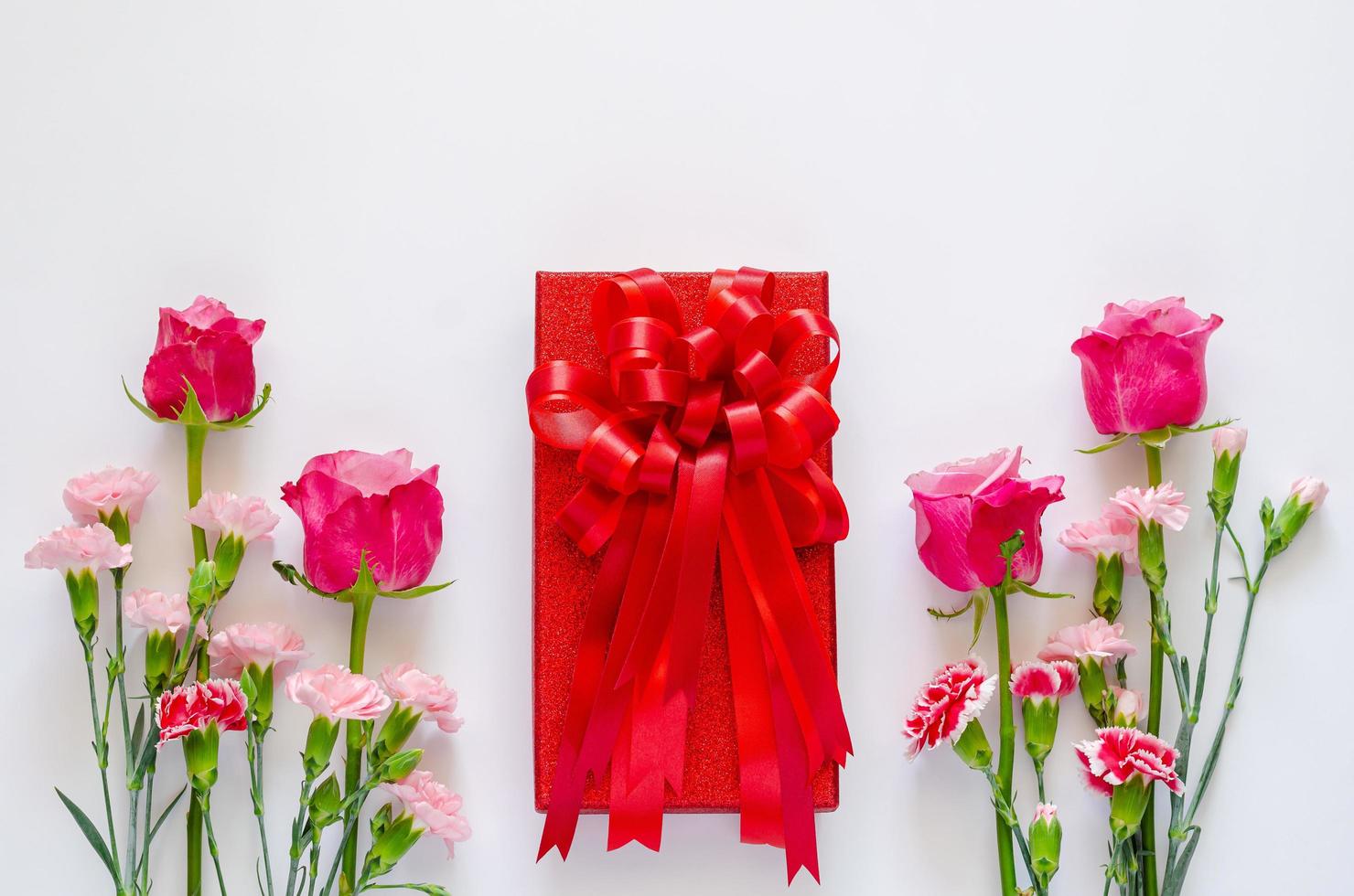 rood geschenk doos met lint en kleurrijk bloemen Aan wit achtergrond voor verjaardag of Valentijn dag concept. foto