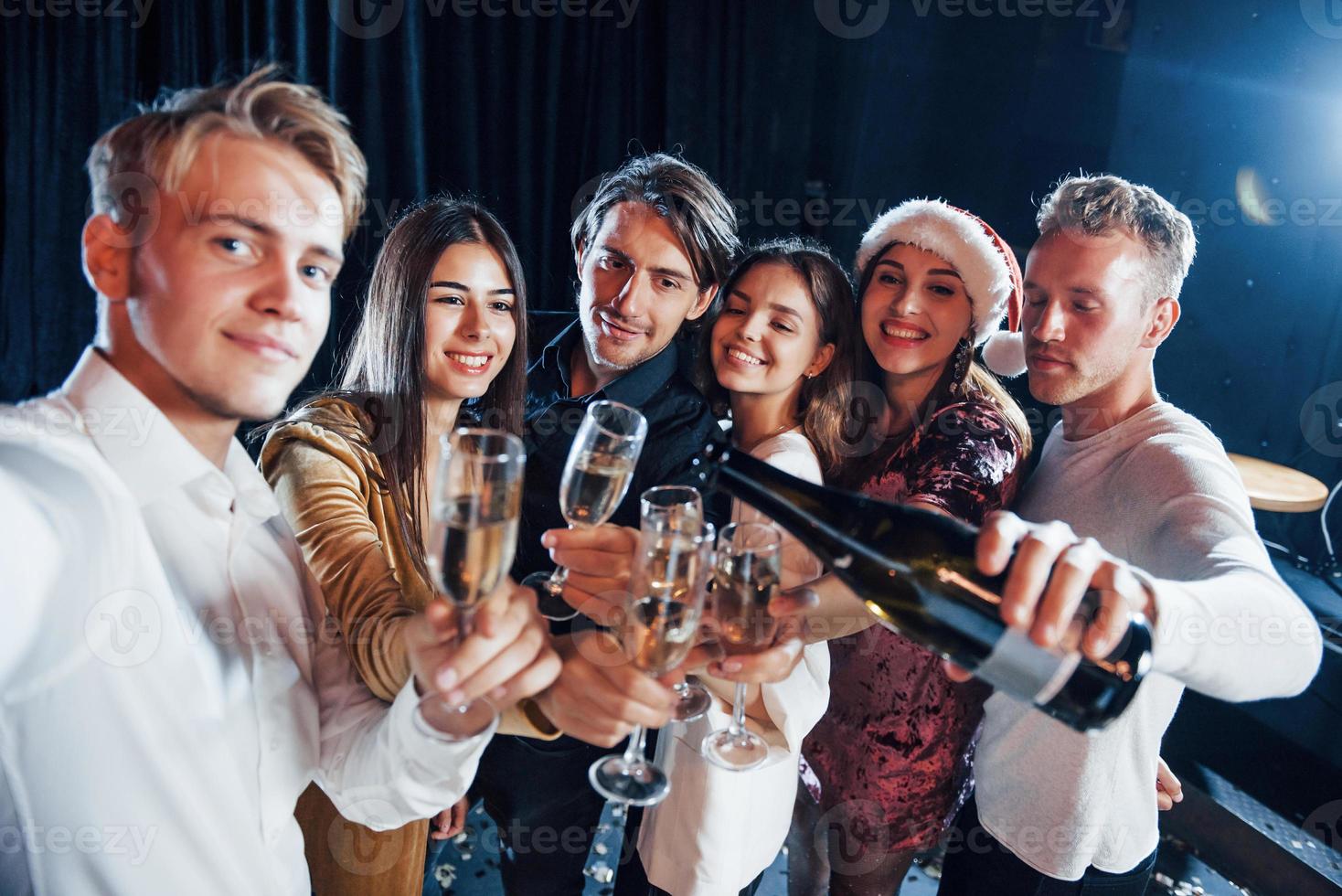 duurt selfie. groep van vrolijk vrienden vieren nieuw jaar binnenshuis met drankjes in handen foto