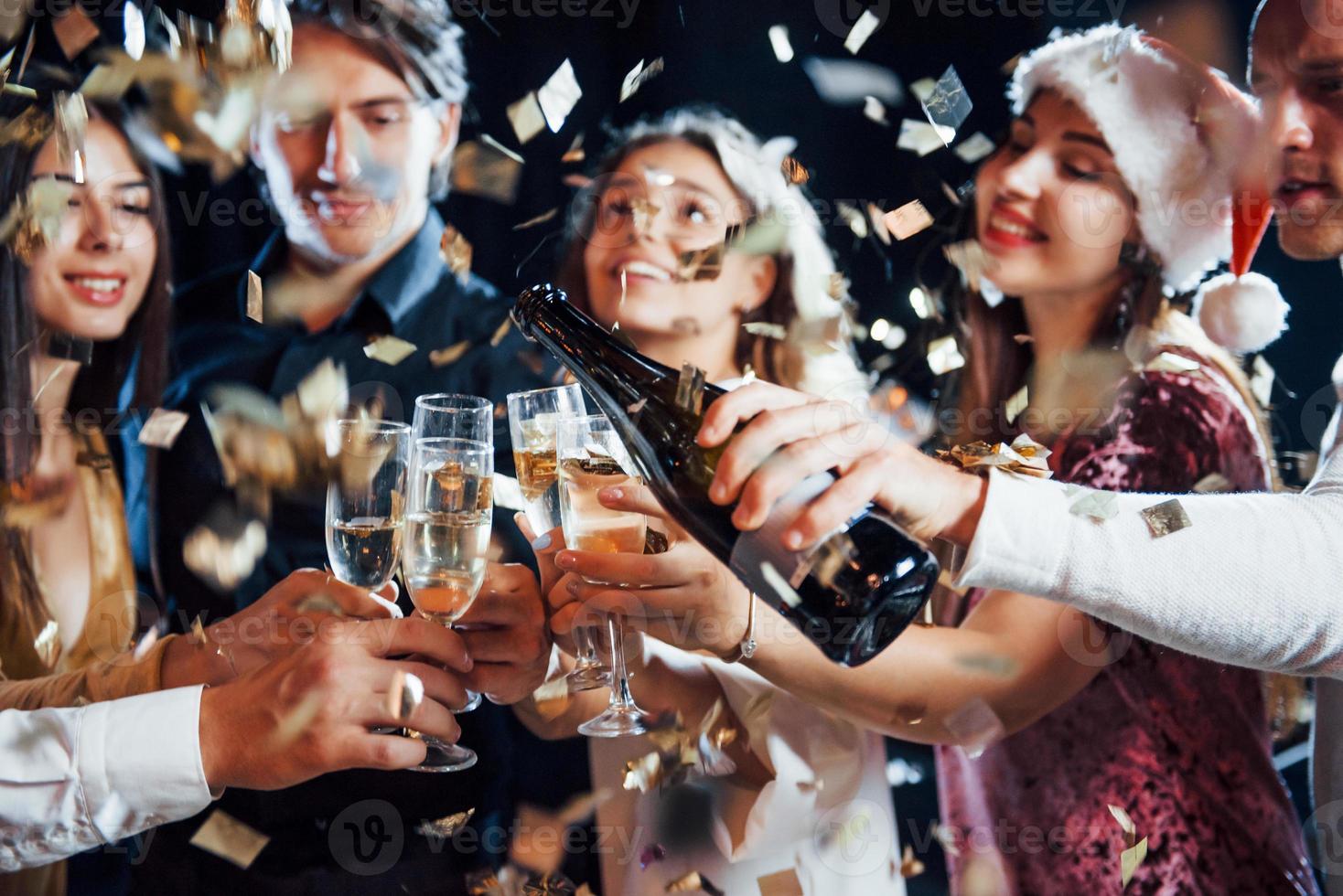 gieten Champagne. groep van vrolijk vrienden vieren nieuw jaar binnenshuis met drankjes in handen foto