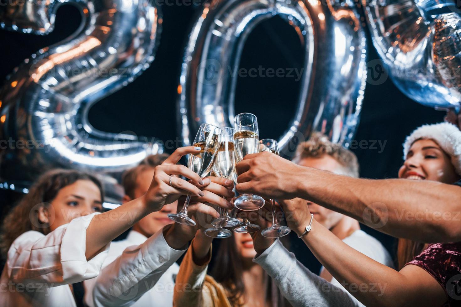 kloppen bril. groep van vrolijk vrienden vieren nieuw jaar binnenshuis met drankjes in handen foto