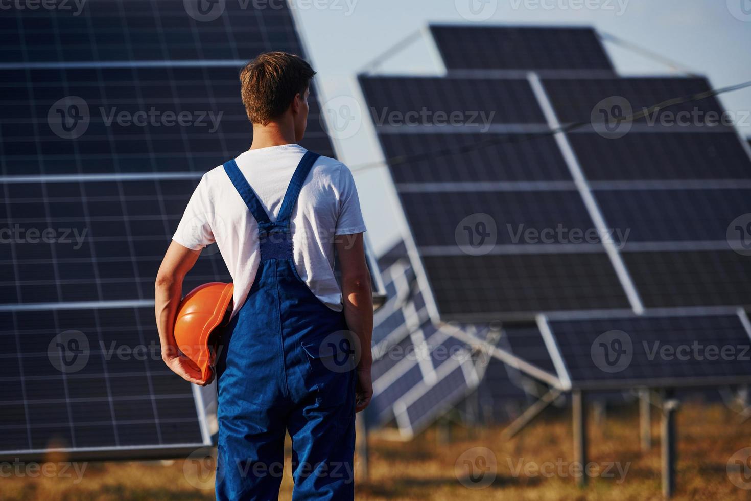 achterzijde visie van mannetje arbeider in blauw uniform buitenshuis met zonne- batterijen Bij zonnig dag foto