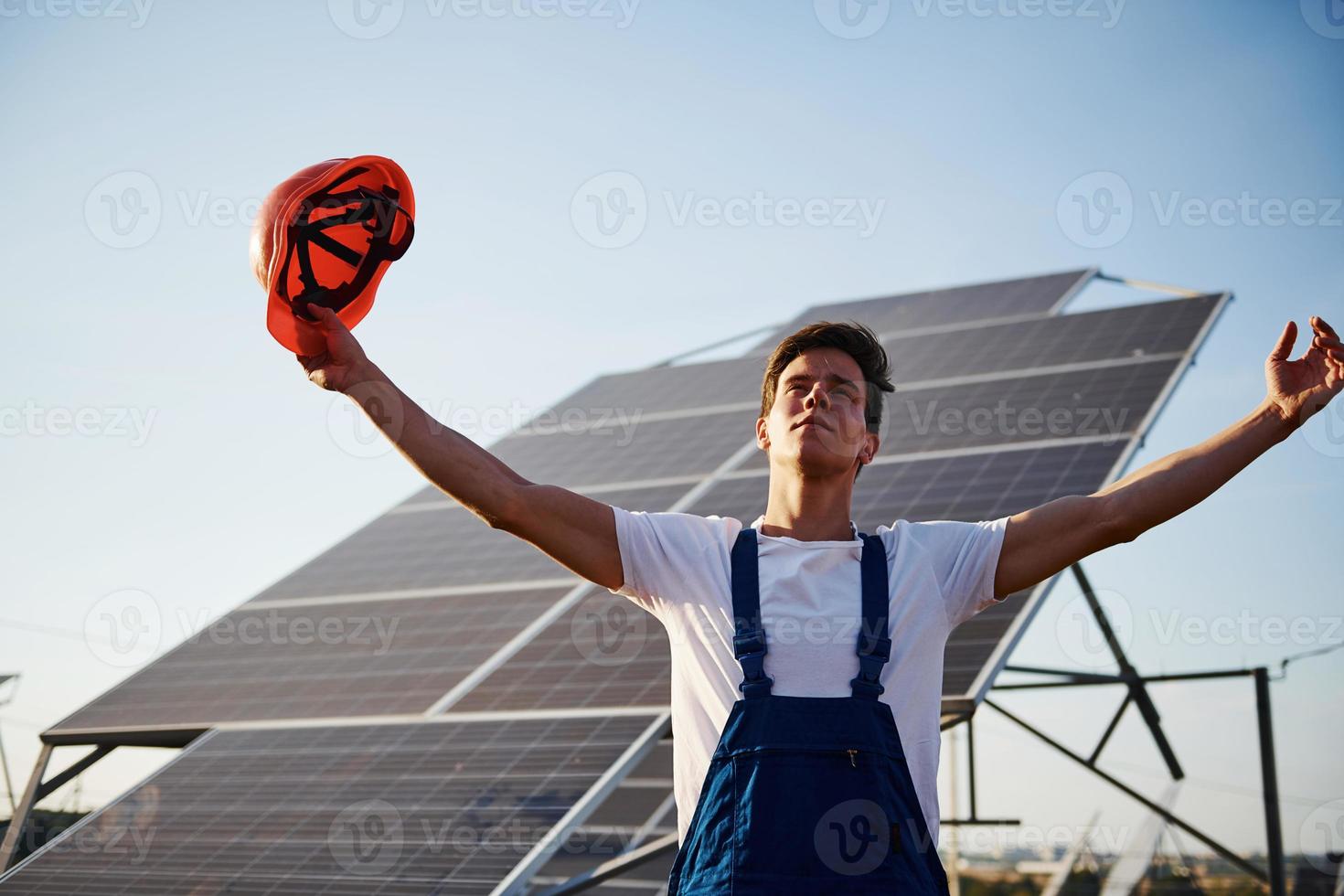 handen verheven omhoog. mannetje arbeider in blauw uniform buitenshuis met zonne- batterijen Bij zonnig dag foto