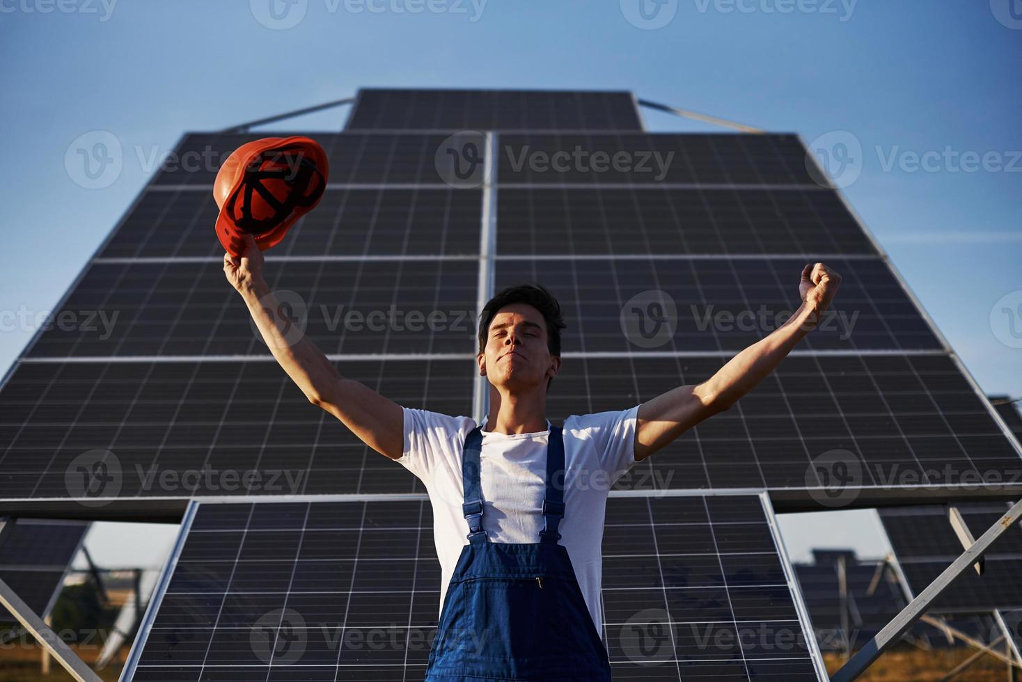 handen verheven omhoog. mannetje arbeider in blauw uniform buitenshuis met zonne- batterijen Bij zonnig dag foto