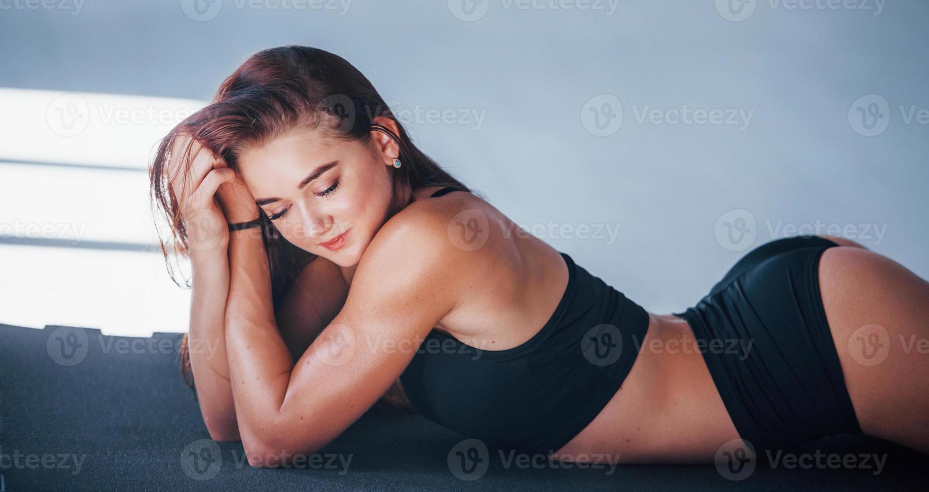 jong vrouw met slank type van lichaam en in zwart sportief kleren aan het liegen naar beneden Aan de geschiktheid mat foto