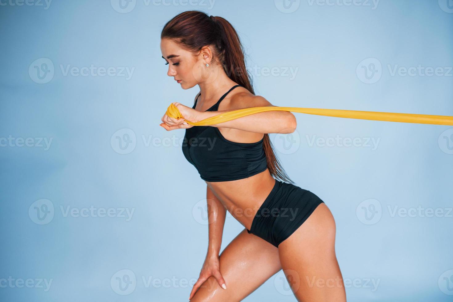 handen oefening door gebruik makend van weerstand band. jong vrouw met slank lichaam type geïsoleerd tegen blauw achtergrond foto