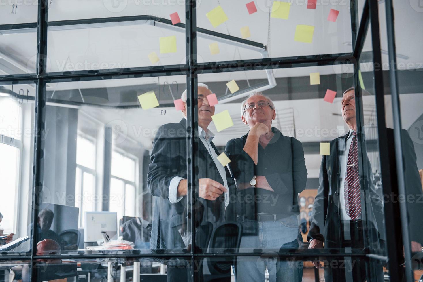 werken met stickers Aan de glas. oud team van ouderen zakenman architecten hebben een vergadering in de kantoor foto