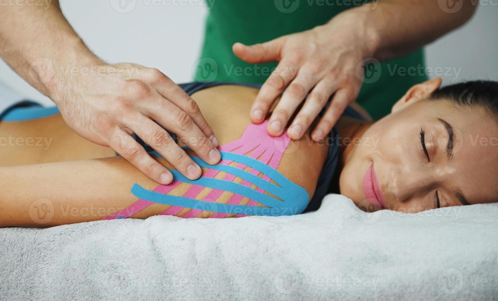 dokter helpt vrouw door schouder behandeling met kinesio plakband foto