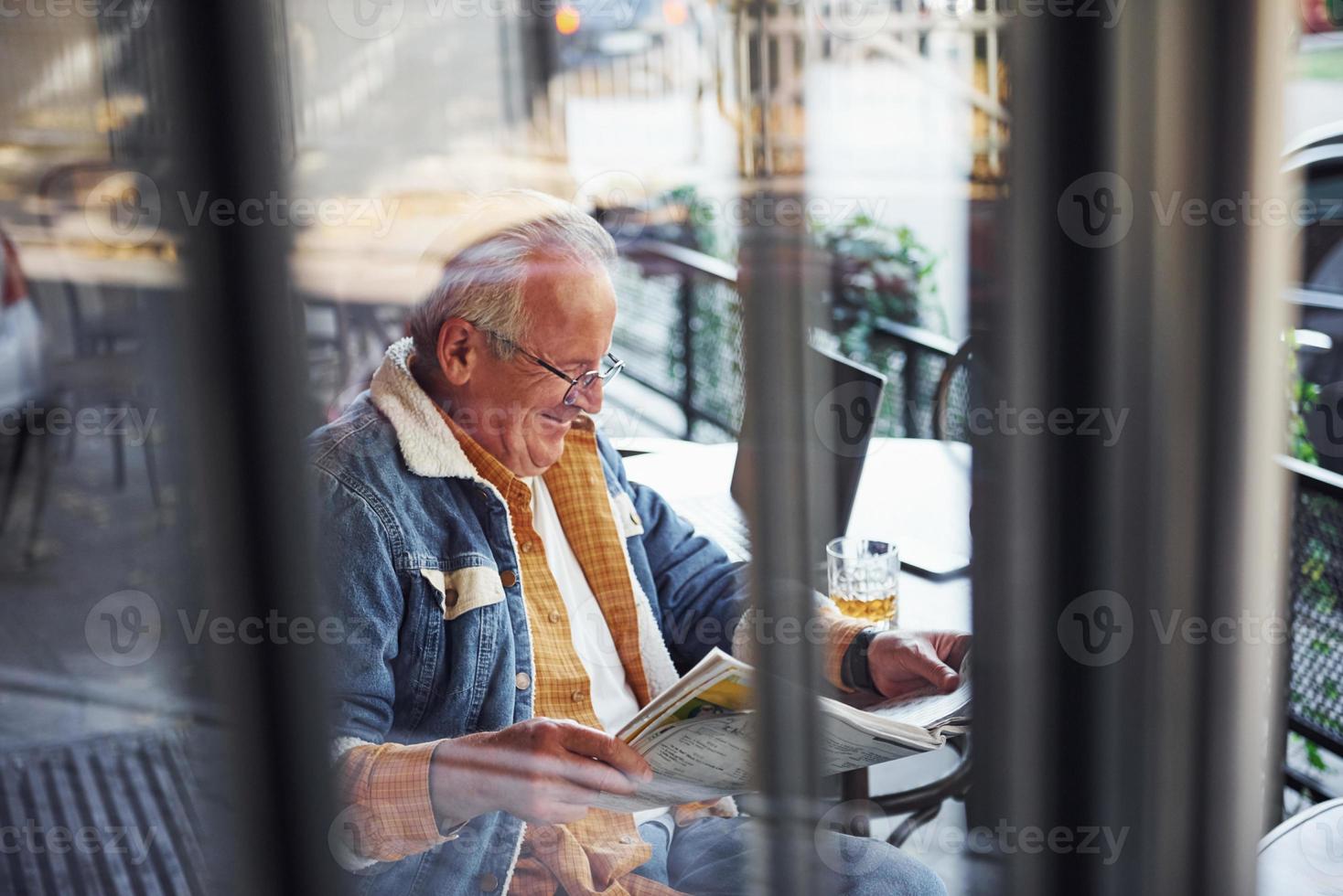 elegant senior in modieus kleren en in bril zit in de cafe en leest krant- foto