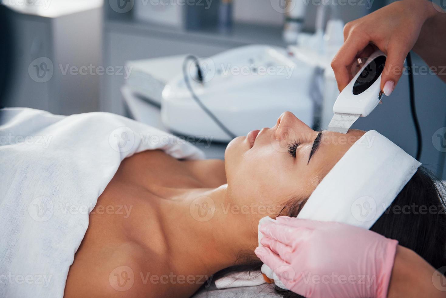 gebruik makend van speciaal apparaat. dichtbij omhoog visie van vrouw dat aan het liegen naar beneden in spa salon en hebben gezicht schoonmaak procedure foto