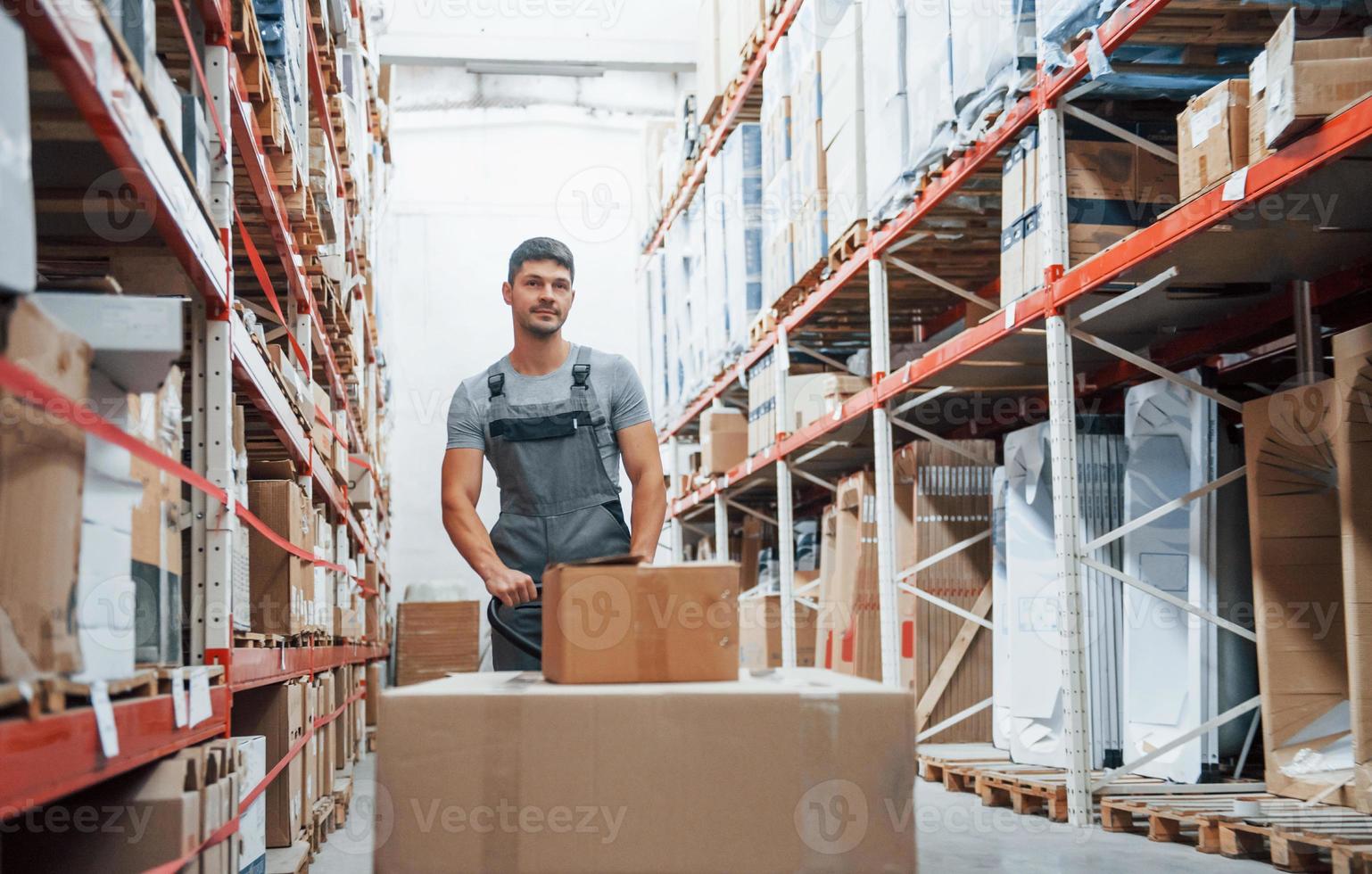 jong mannetje arbeider in uniform is in de magazijn voortvarend pallet vrachtauto foto