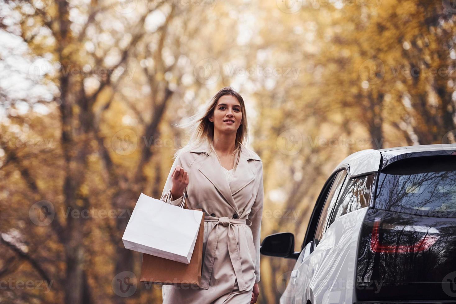 meisje wandelingen in de buurt de auto met boodschappen doen Tassen in handen. modern merk nieuw auto- in de Woud foto