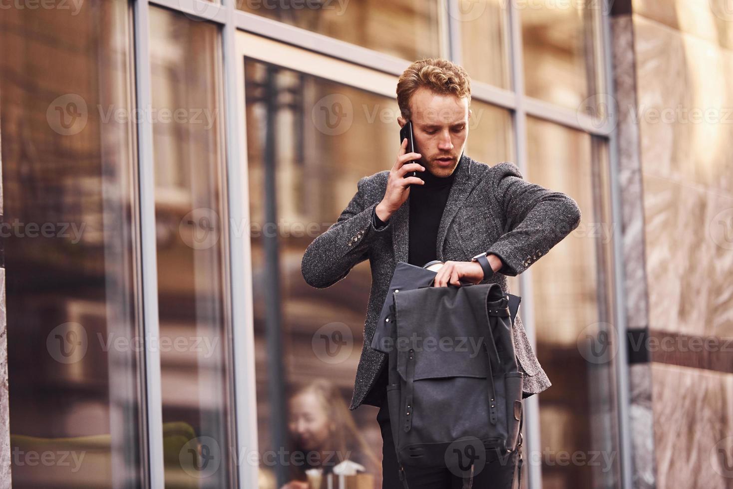 Mens in elegant formeel slijtage buiten tegen modern gebouw pratend door de telefoon foto