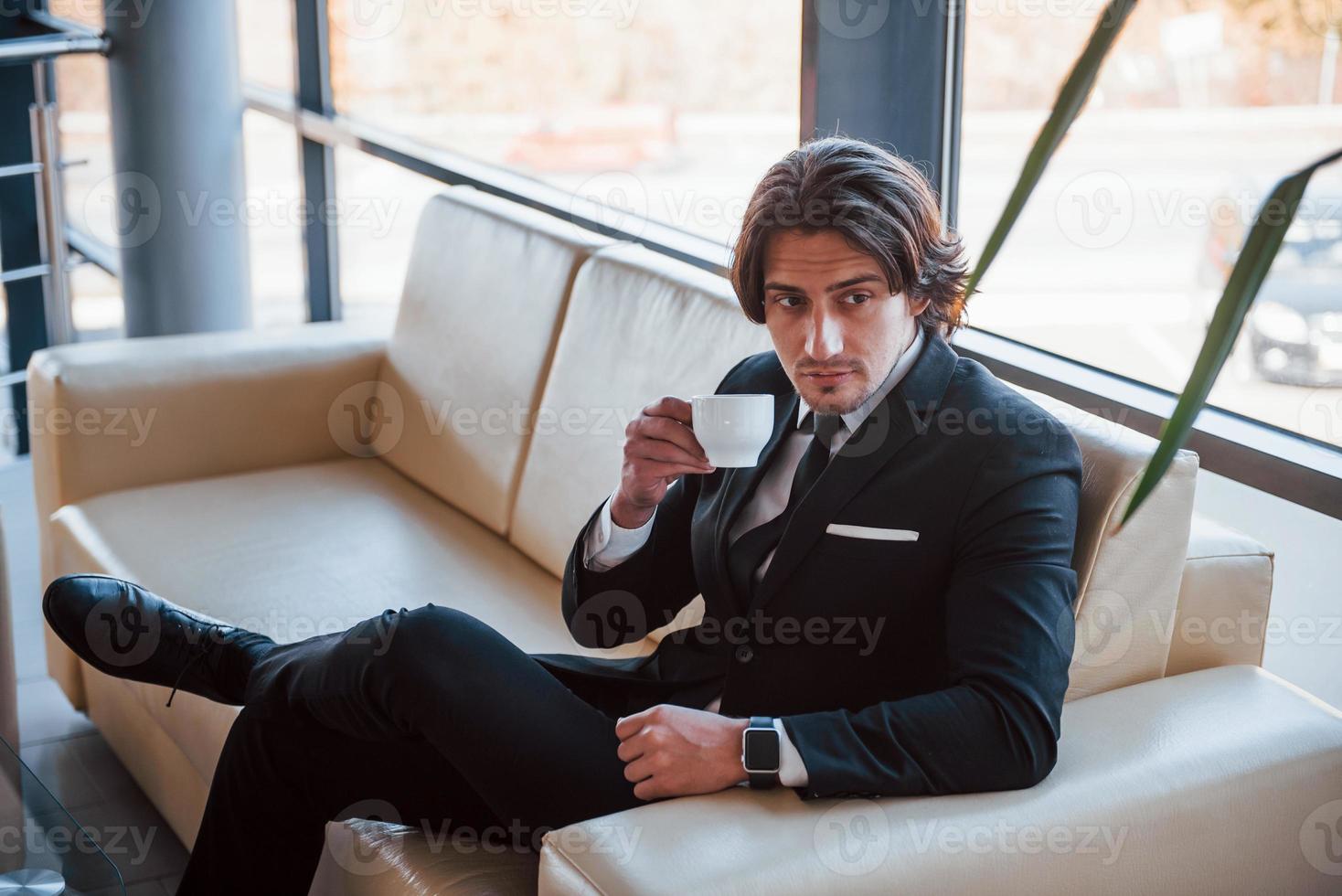 portret van knap jong zakenman in zwart pak en stropdas dat zit Aan de sofa en duurt een breken foto