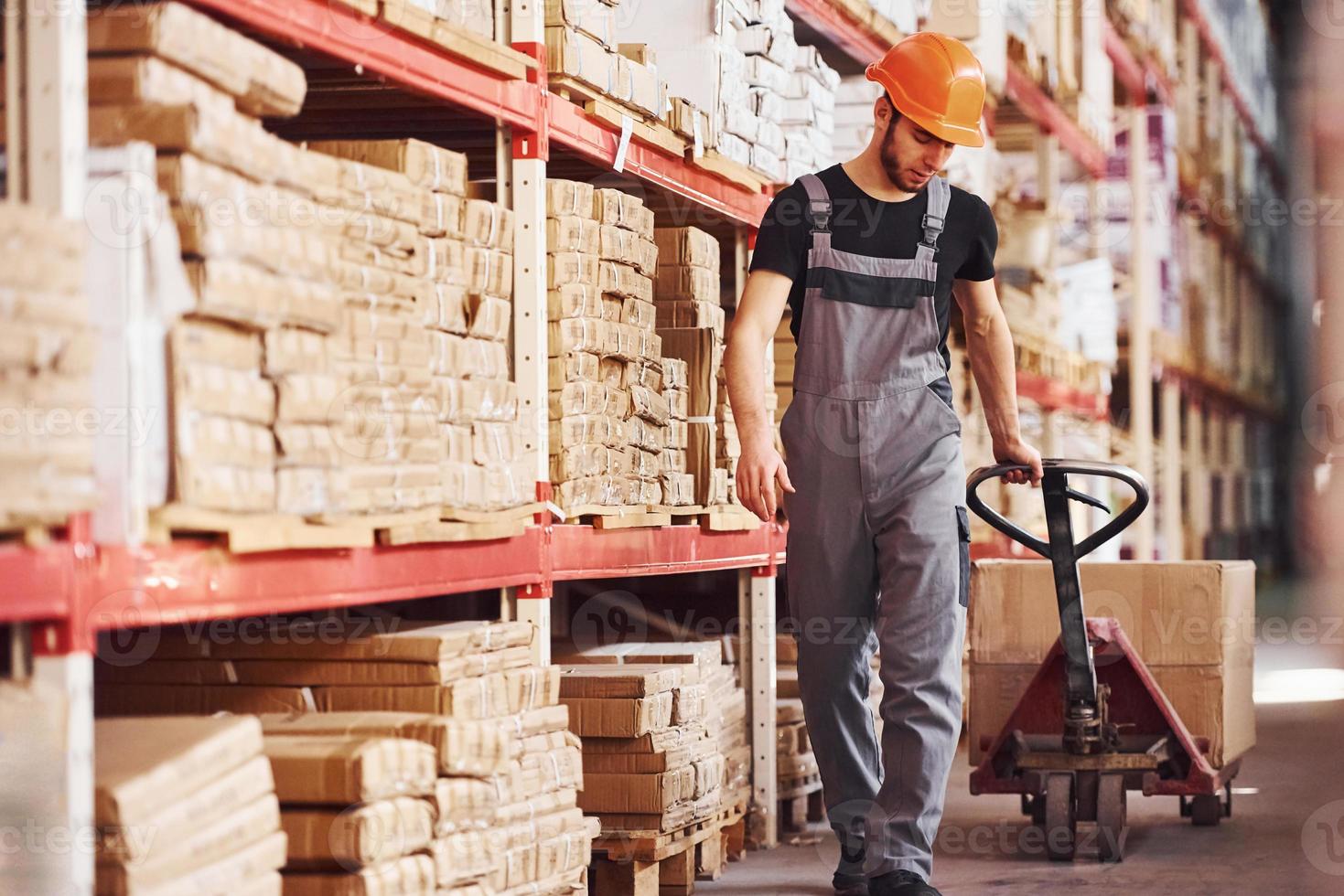 jong mannetje arbeider in uniform is in de magazijn voortvarend pallet vrachtauto foto