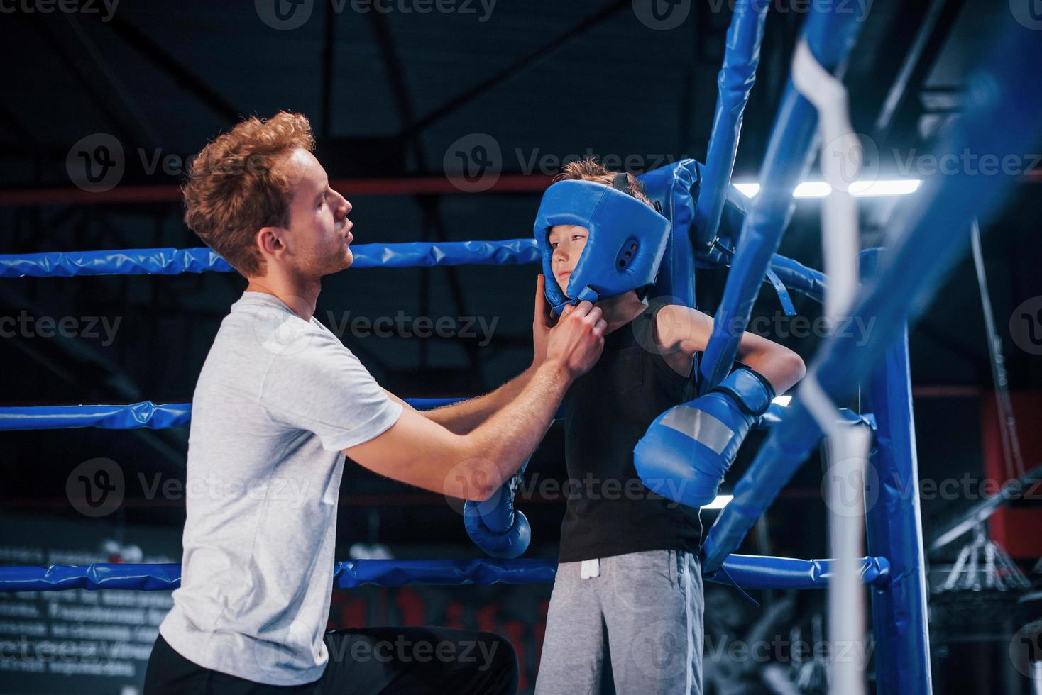 jong boksen trainer is helpen weinig jongen in beschermend slijtage Aan de ring tussen de rondes foto