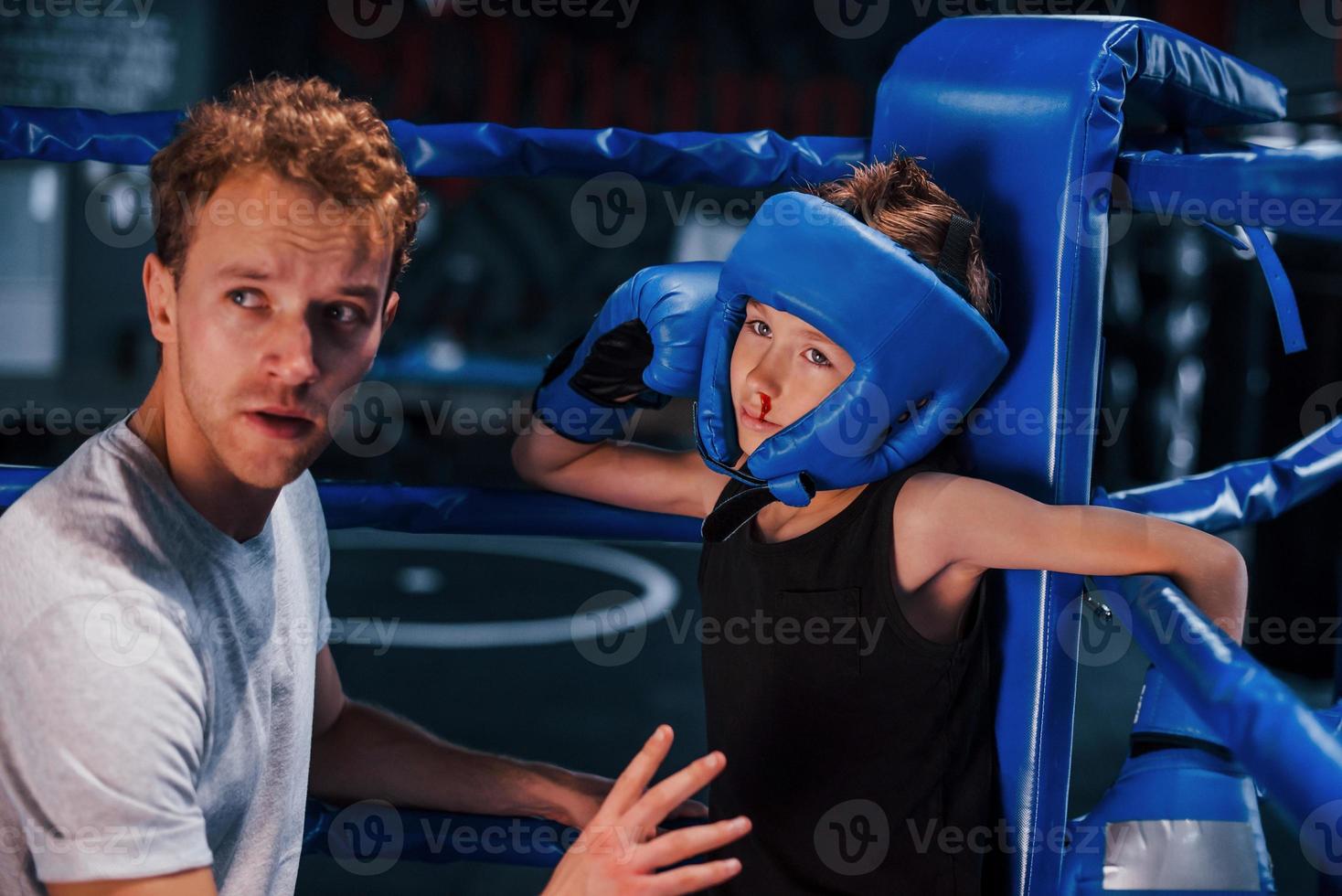 jong boksen trainer is helpen weinig jongen in beschermend slijtage Aan de ring tussen de rondes foto