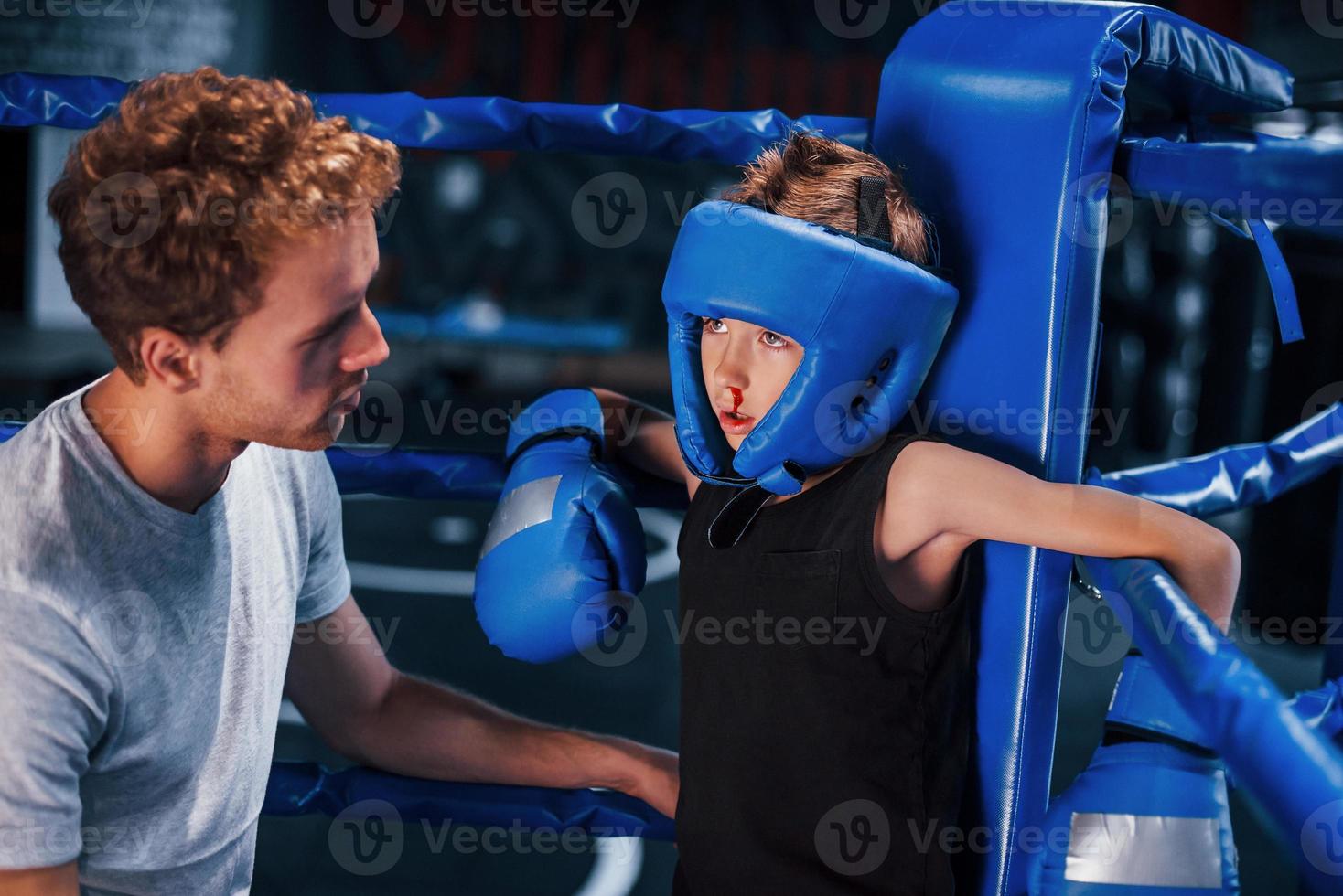 jong boksen trainer is helpen weinig jongen in beschermend slijtage Aan de ring tussen de rondes foto