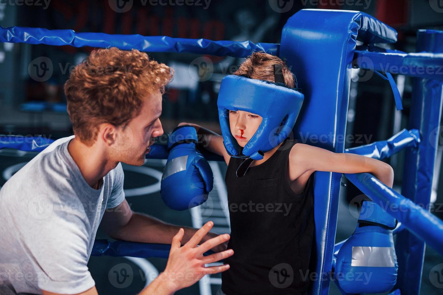 jong boksen trainer is helpen weinig jongen in beschermend slijtage Aan de ring tussen de rondes foto