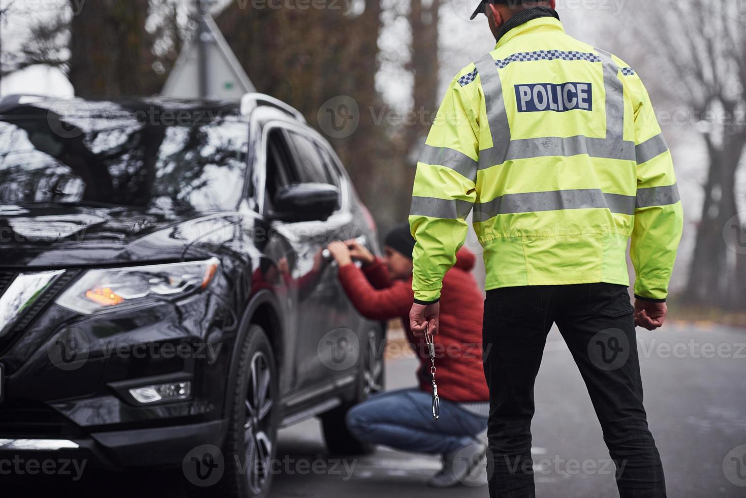 Politie officier in groen uniform gevangen auto- diefstal Aan de weg foto