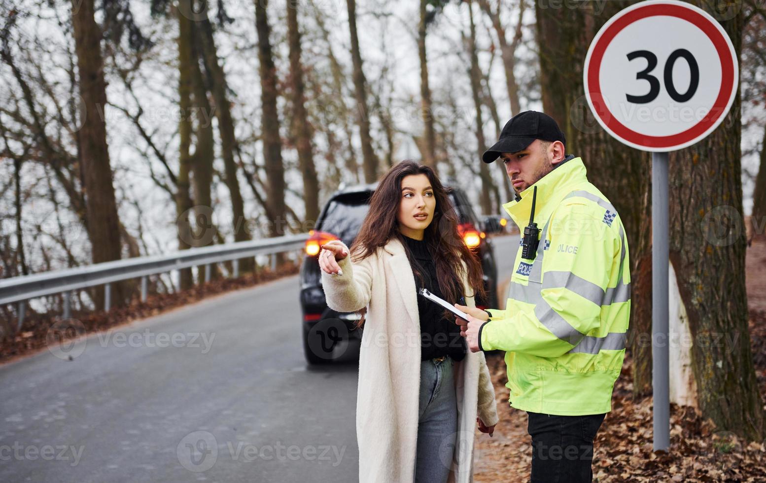 mannetje Politie officier in groen uniform pratend met vrouw eigenaar van de auto Aan de weg foto
