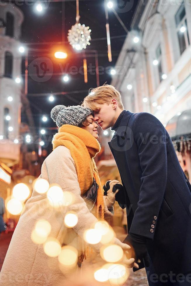 jong paar in warm kleren zoenen Aan Kerstmis versierd straat foto