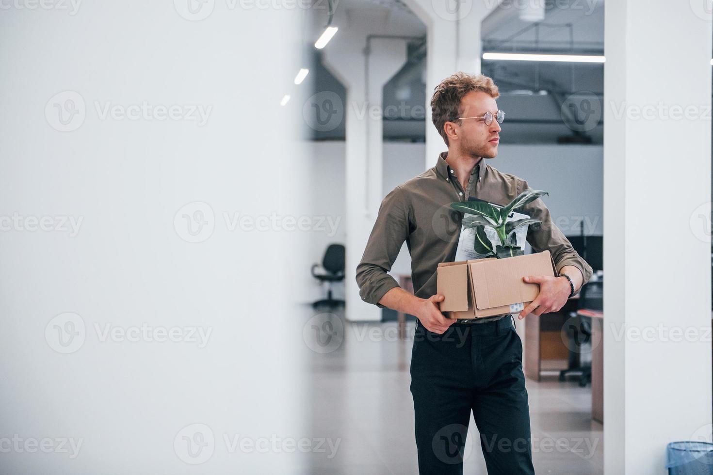 kantoor arbeider in formeel slijtage wandelen met doos met groen fabriek binnen van het foto