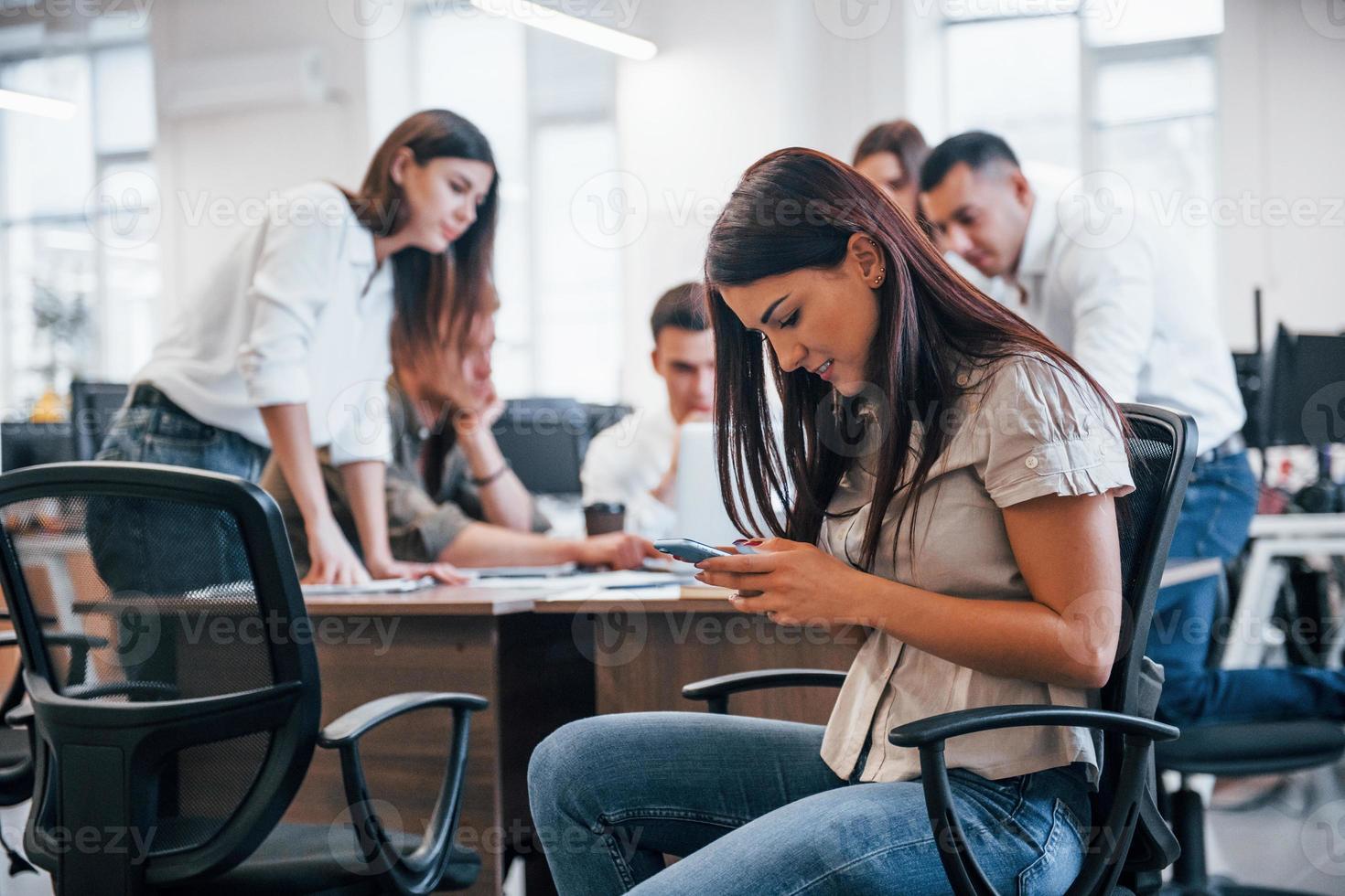 knap vrouw met telefoon is in de kantoor. groep van mensen werken Bij project achter foto