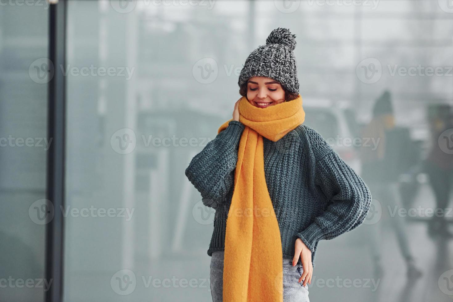 mooi vrolijk meisje in geel sjaal en in warm kleren staand binnenshuis tegen achtergrond met reflecties foto