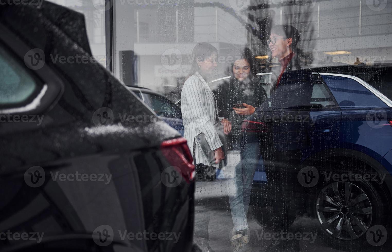 vrienden staand achter glas Bij regenachtig dag. meisje houdt laptop in handen foto