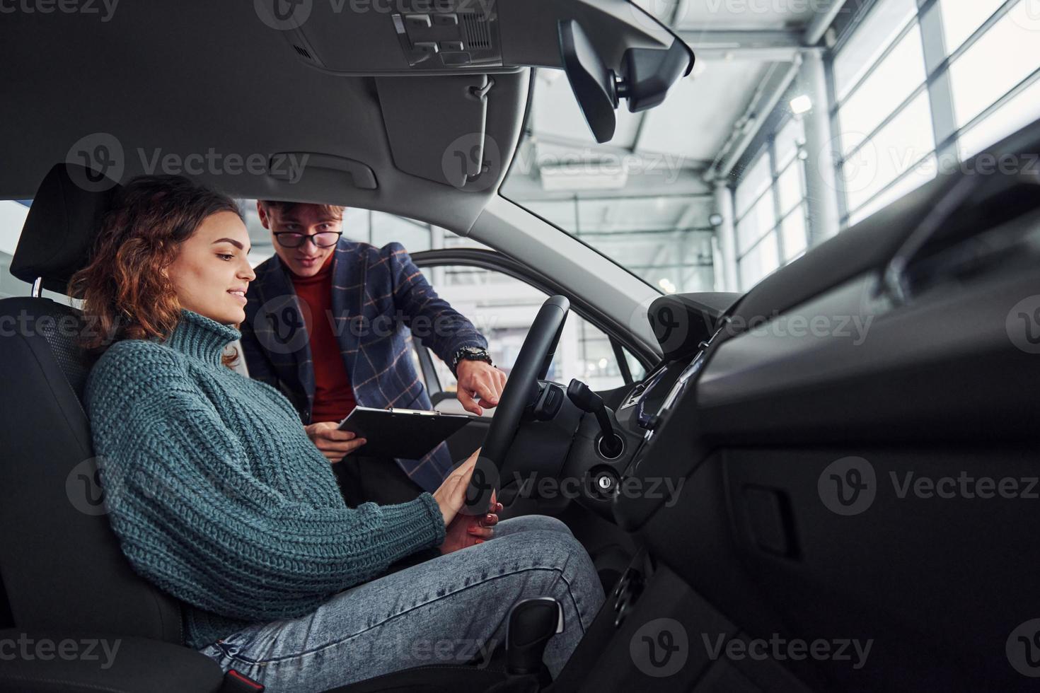 professioneel verkoper assisteren jong meisje door kiezen nieuw modern auto- binnenshuis. vrouw zittend binnen foto