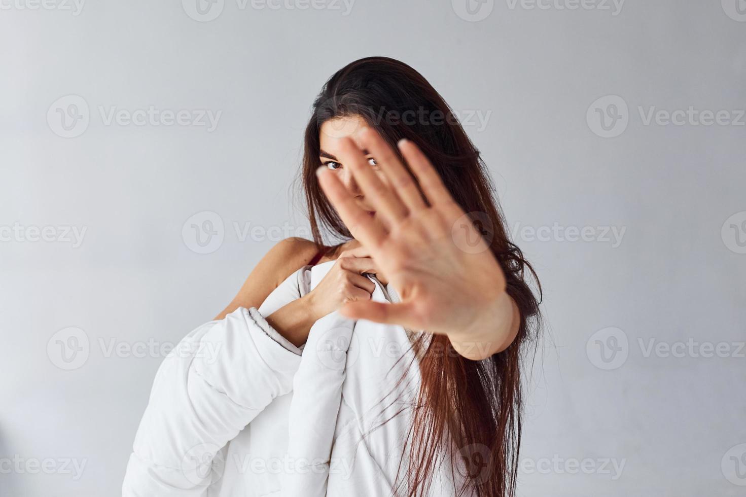 hou op gebaar. vrouw aan het bedekken haar lichaam door handdoek in de studio tegen wit achtergrond foto