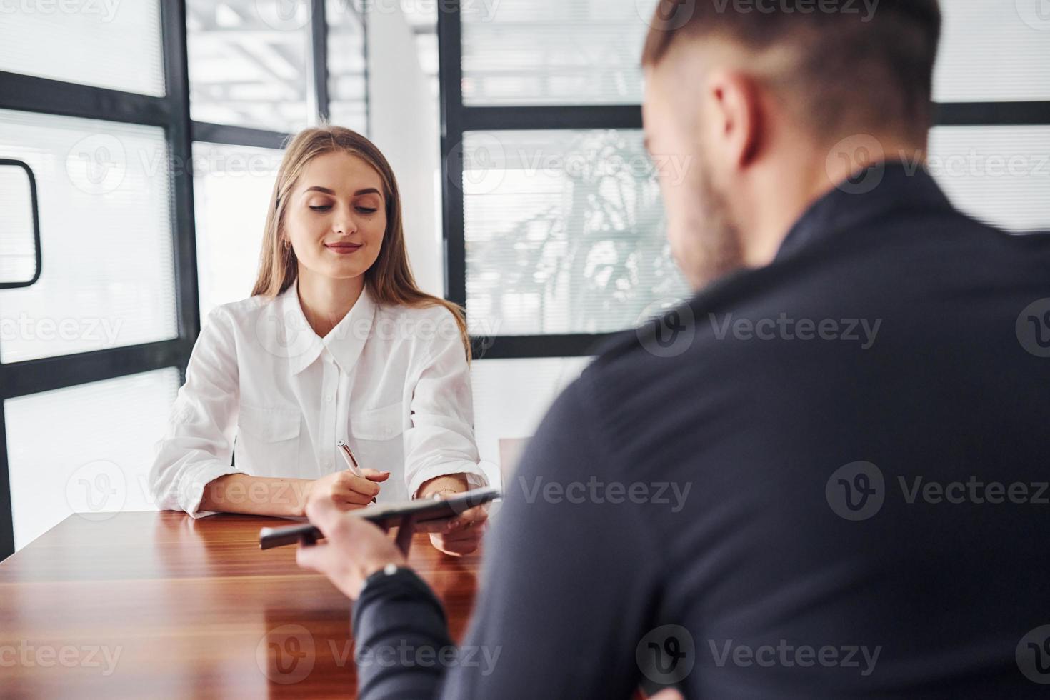 achterzijde visie. vrouw en Mens in formeel kleren werken samen binnenshuis in de kantoor door tafel foto