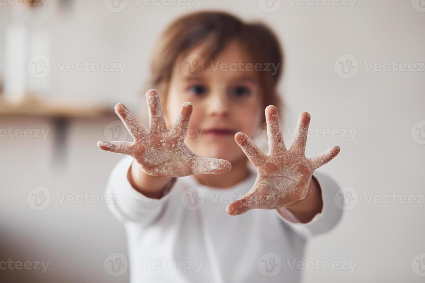 positief weinig meisje tonen handen met meel Aan in Aan de keuken foto