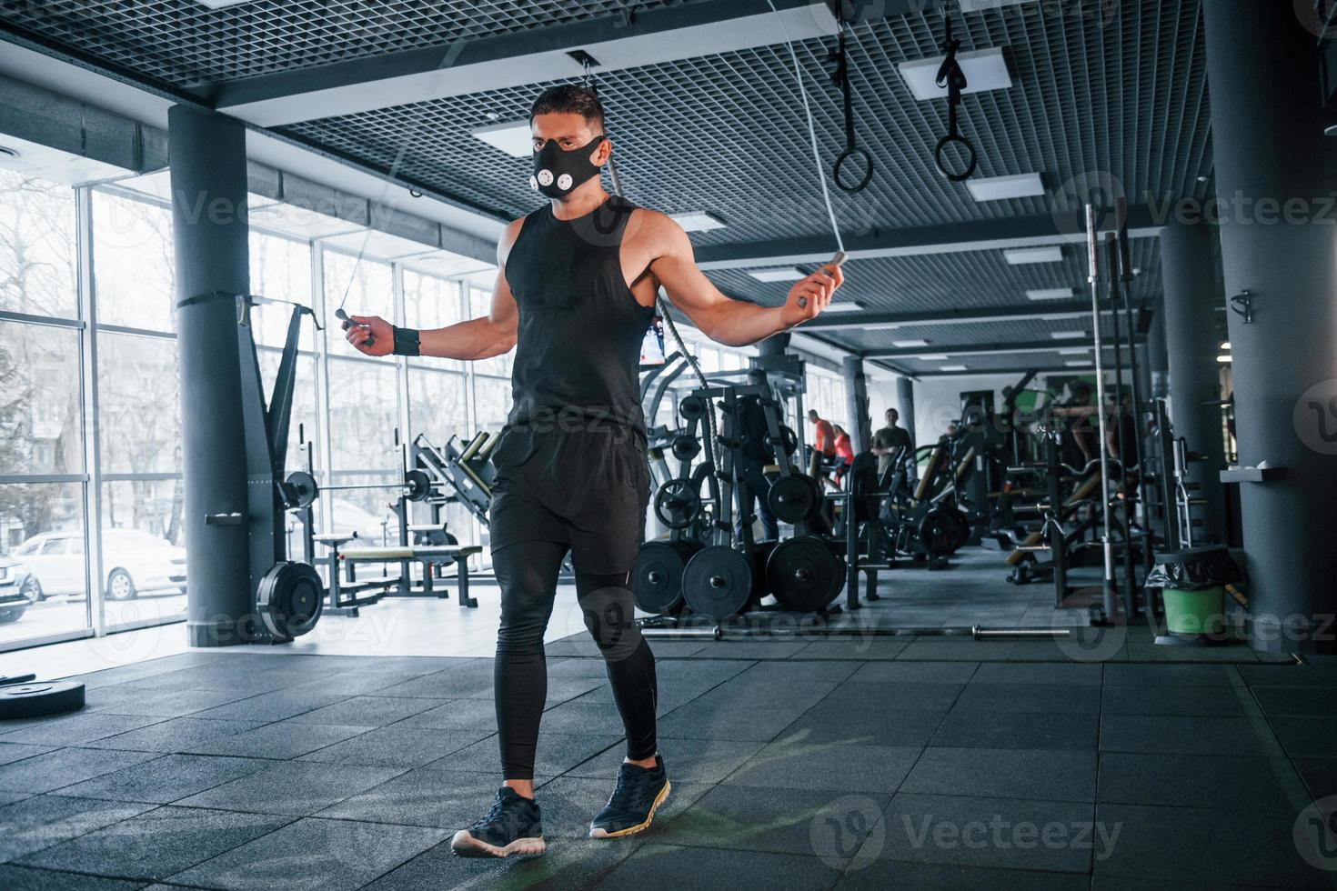 sterk jong Mens in sportief kleren en eng masker aan het doen oefening door gebruik makend van springen touw in Sportschool foto