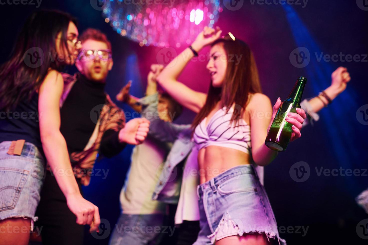 meisje Holding fles. jong mensen is hebben pret in nacht club met kleurrijk laser lichten foto