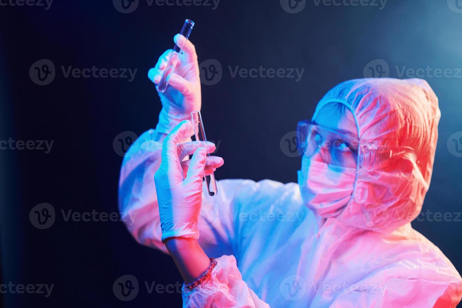 verpleegster in masker en wit uniform staand in neon verlicht kamer en Holding buizen met monsters foto