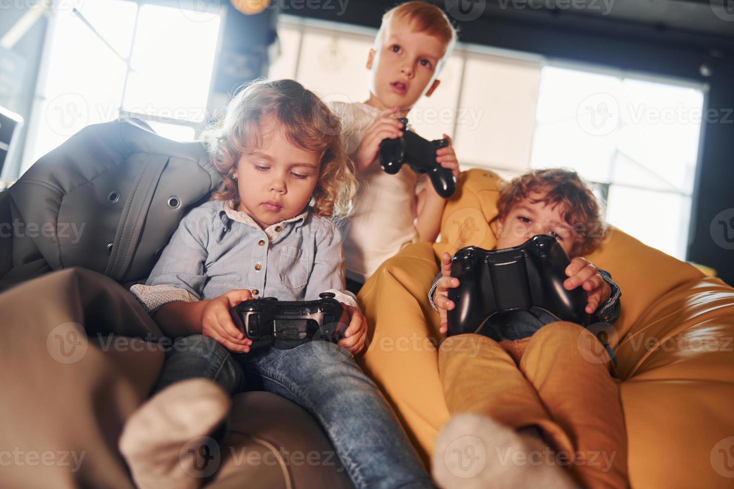kinderen in gewoontjes kleren zittend samen met controleur en spelen video spellen foto