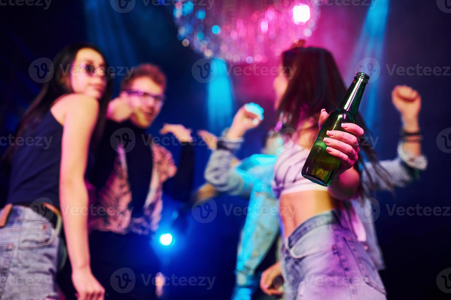 meisje Holding fles. jong mensen is hebben pret in nacht club met kleurrijk laser lichten foto