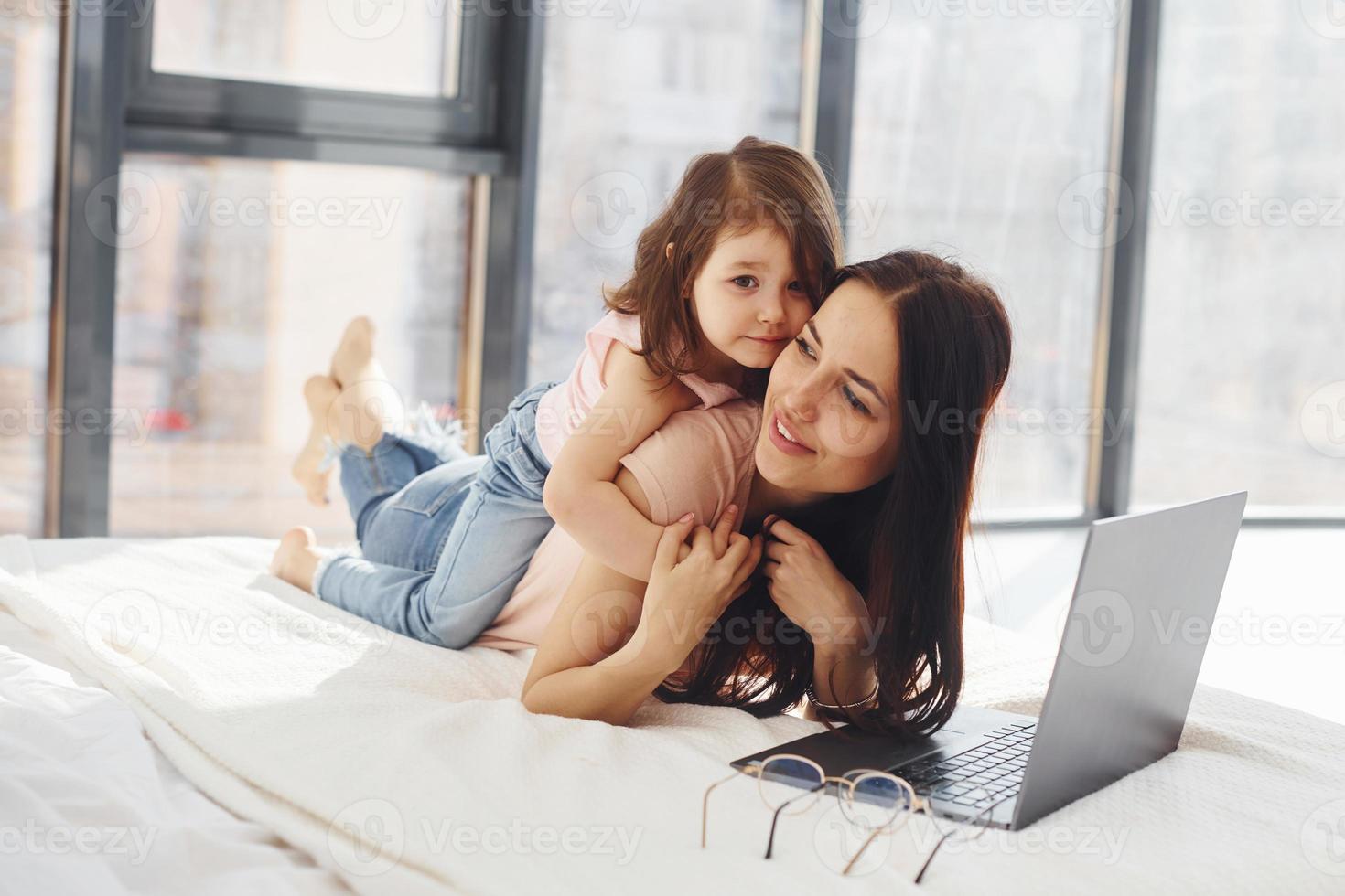 jong moeder met haar dochter uitgeven weekend samen in kamer en gebruik makend van laptop foto