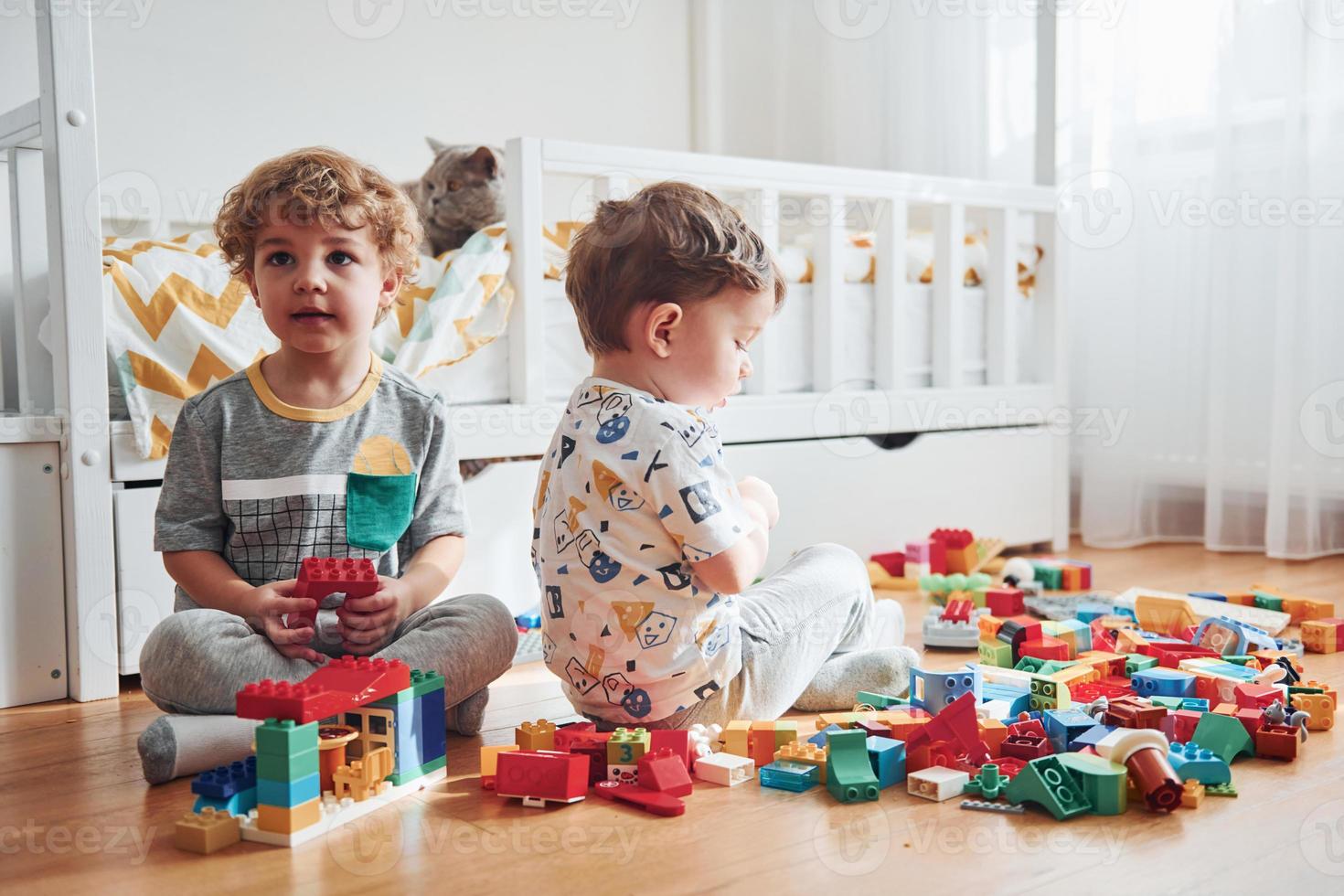 twee weinig jongens hebben pret binnenshuis in de slaapkamer met plastic bouw set. kat zit achter hen foto