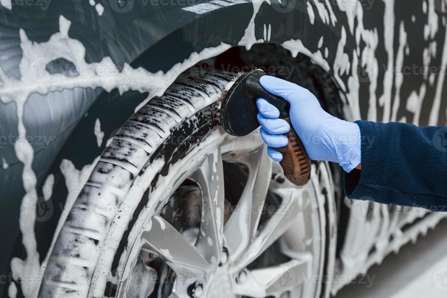 mannetje arbeider in uniform het wassen nieuw modern auto dat gedekt met zeep. opvatting van onderhoud foto