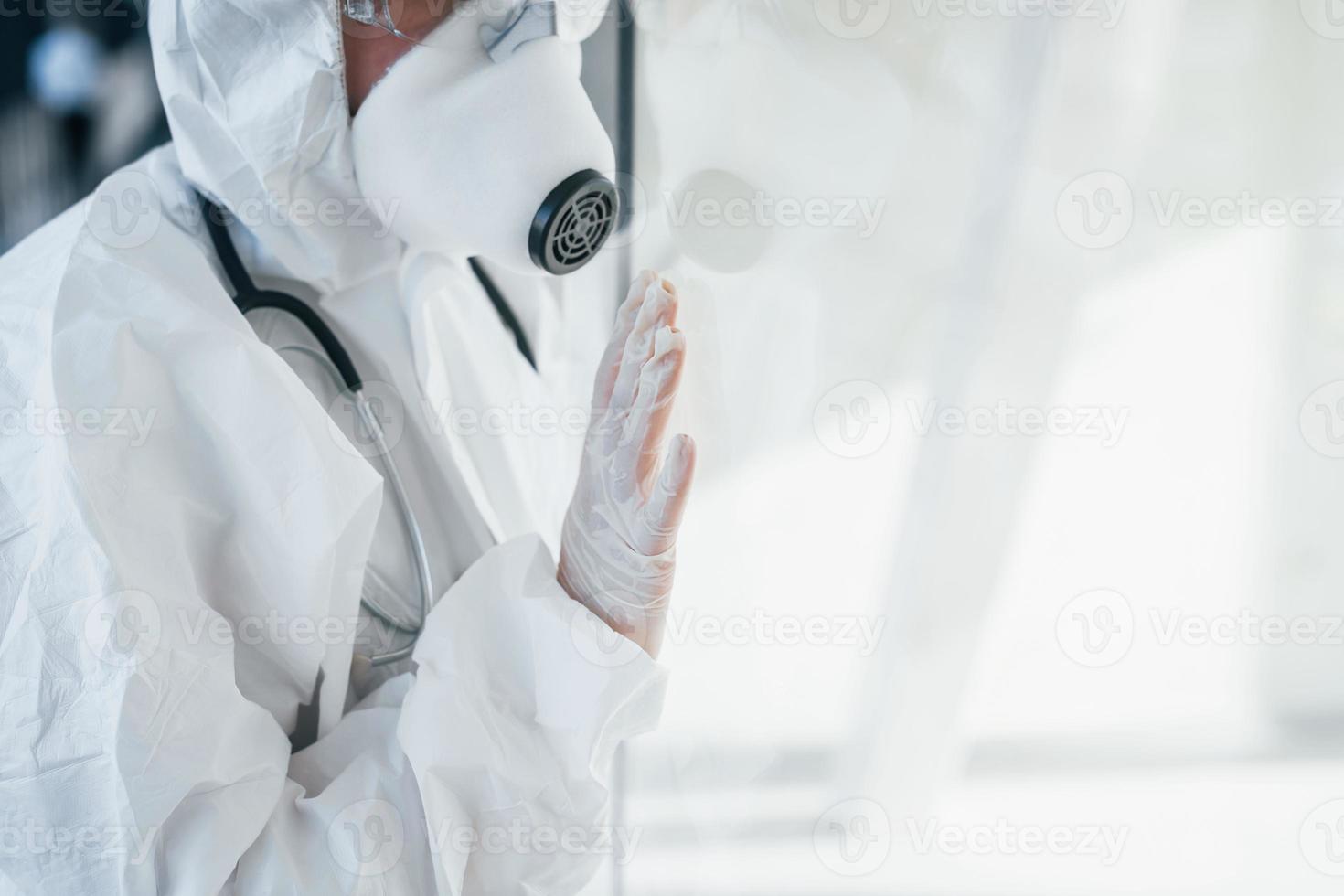 voelt slecht en ziek. vrouw dokter wetenschapper in laboratorium jas, defensief eyewear en masker staand binnenshuis foto