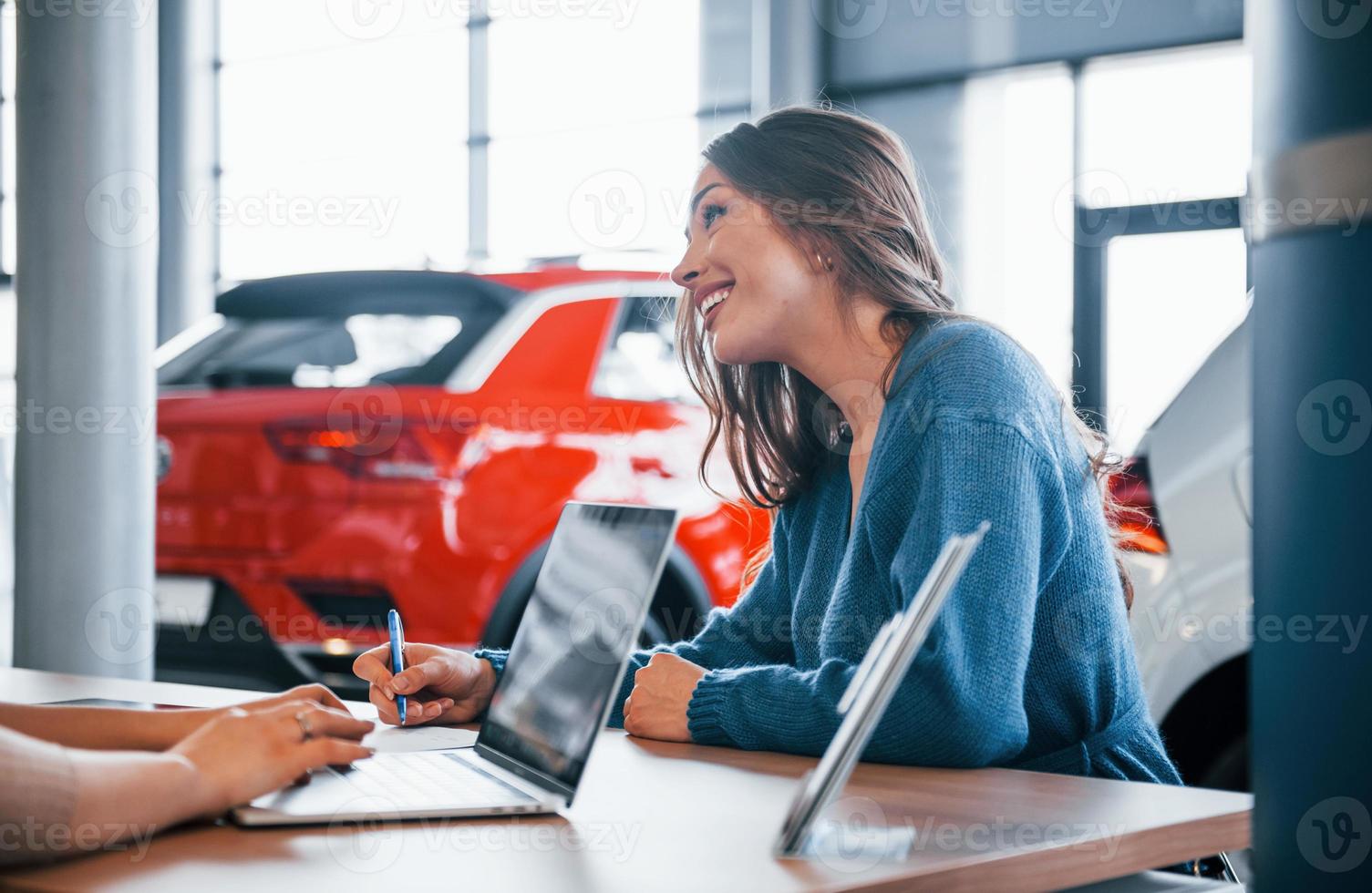 vrolijk vrouw zit met assistent in auto winkel en buying nieuw voertuig foto