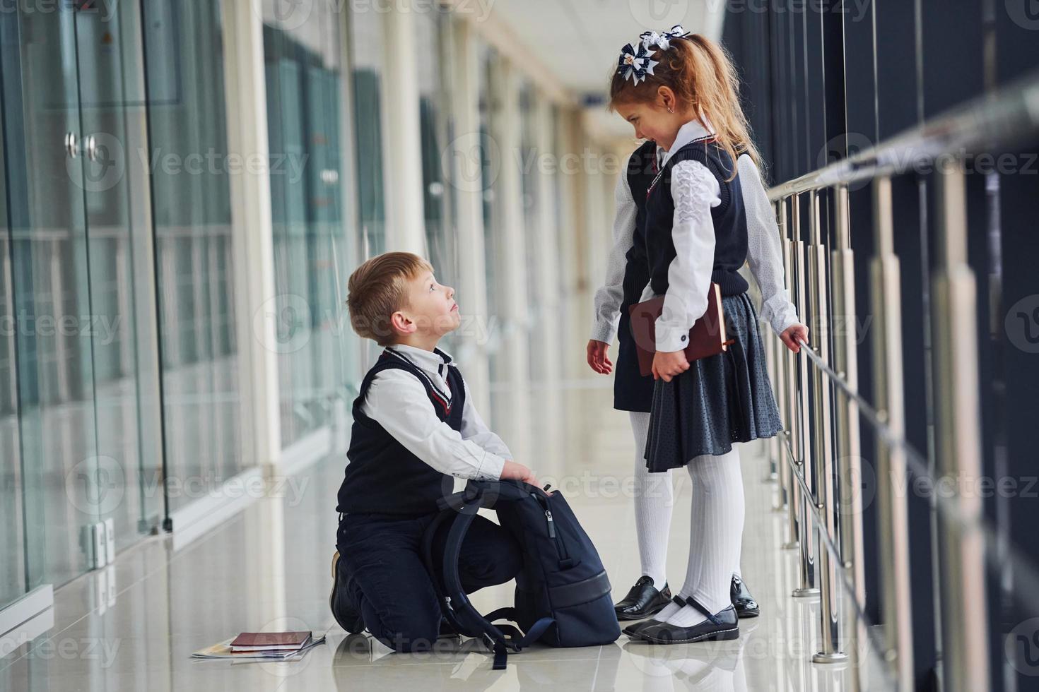 jongen zittend Aan de vloer. school- kinderen in uniform samen in gang foto