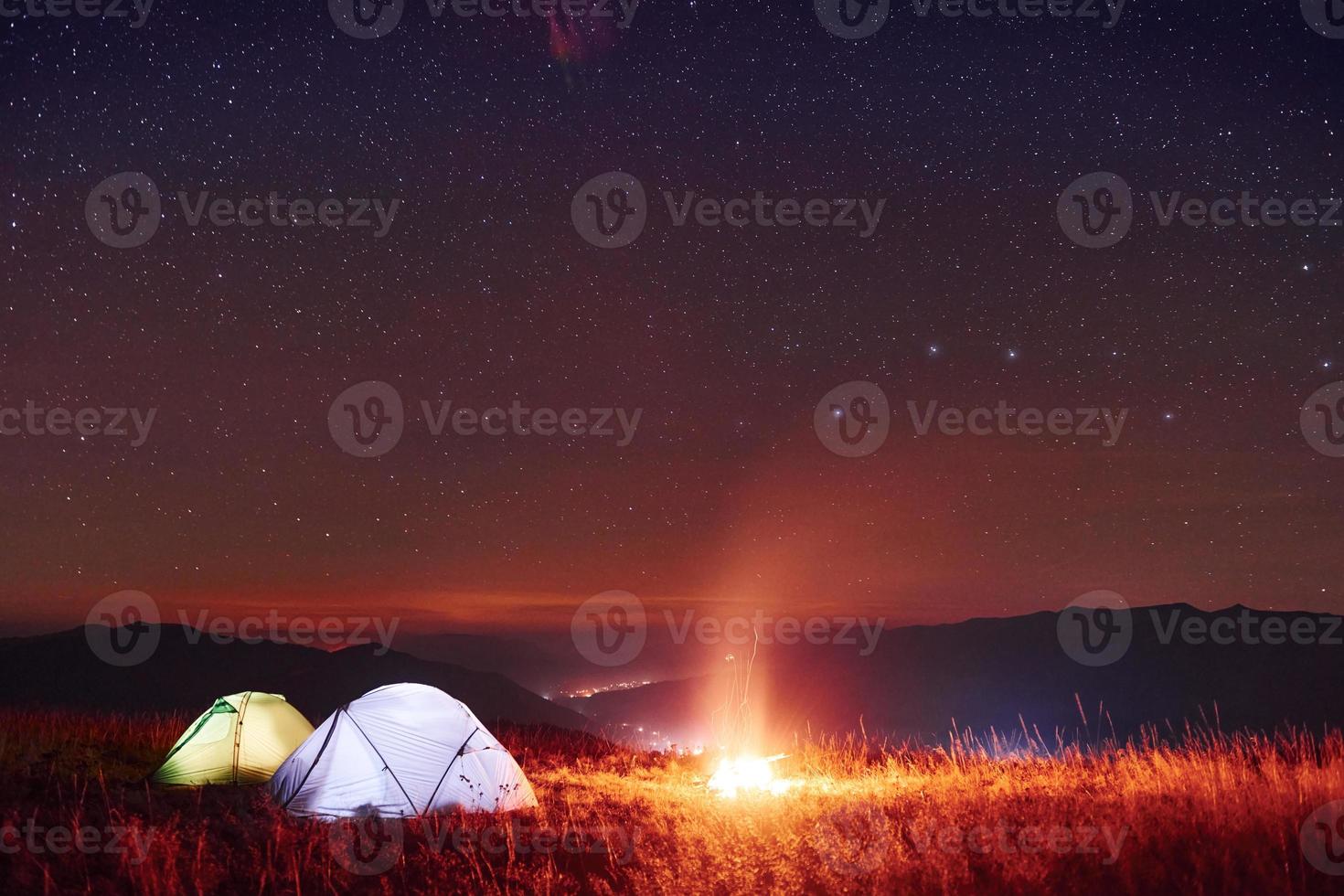 twee verlicht tenten met kampvuur onder sterren Bij bergen Bij nacht foto