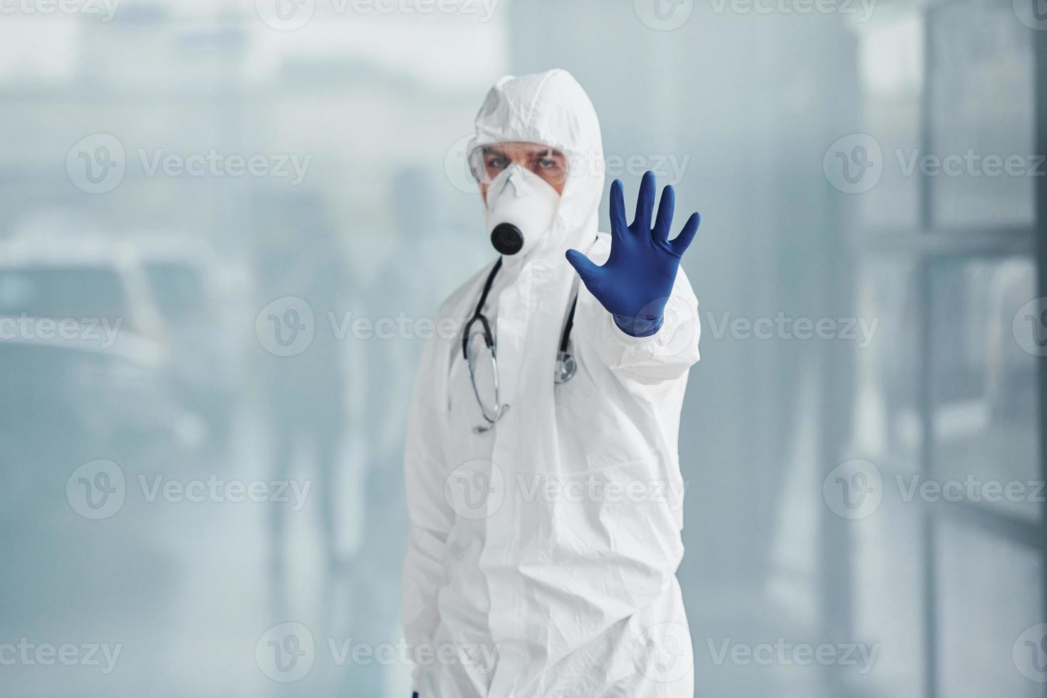 shows hou op gebaar door hand. mannetje dokter wetenschapper in laboratorium jas, defensief eyewear en masker foto