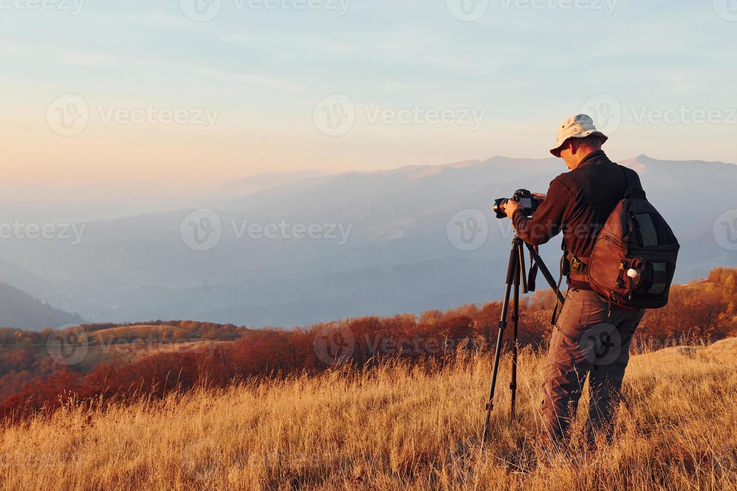 mannetje fotograaf staand en werken Bij majestueus landschap van herfst bomen en bergen door de horizon foto