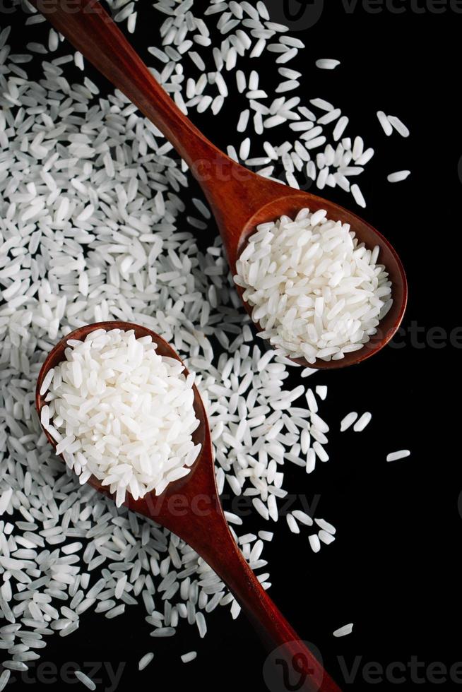wit rauw rijst- in houten lepels Aan zwart achtergrond. natuurlijk biologisch veganistisch voedsel. foto